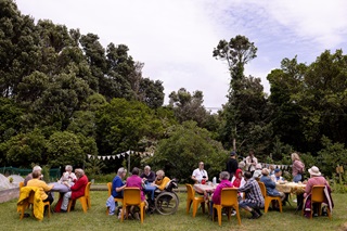 People sit around four tables having a meal at one of our community gardens.