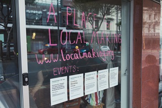 A large glass sliding door with the words 'A place for local making' along with a website written on with pink pen.