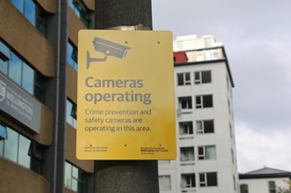 A yellow CCTV camera sign with writing that says 'Cameras operating. Crime prevention and safety cameras are operating in this area.'