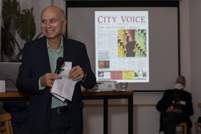 Simon Collins speaking in front of a projector with an image of a City Voice paper on it.