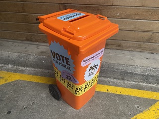 Ballot box bright orange bin with stickers on for election.