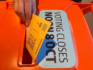 A hand putting a voting form into a ballot box.