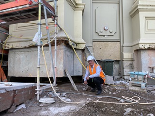 Person crouching outside of the town hall wearing safety gear.