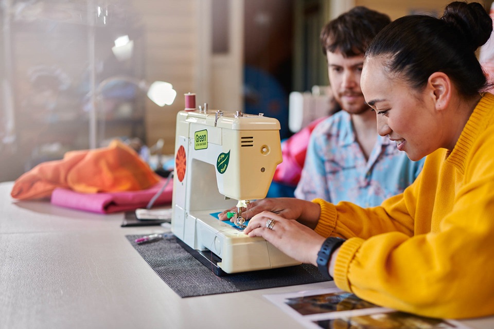 Two young people making clothes with a sewing machine.