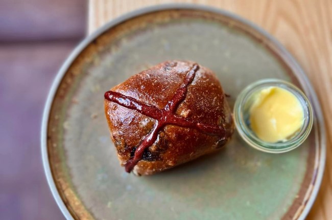 Hot cross bun on a plate with butter.