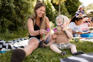A woman and her child sitting on a picnic mat outdoors.