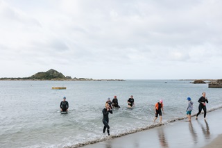 Group of women walking out of the ocean onto the beach with Taputeranga Island in the background.