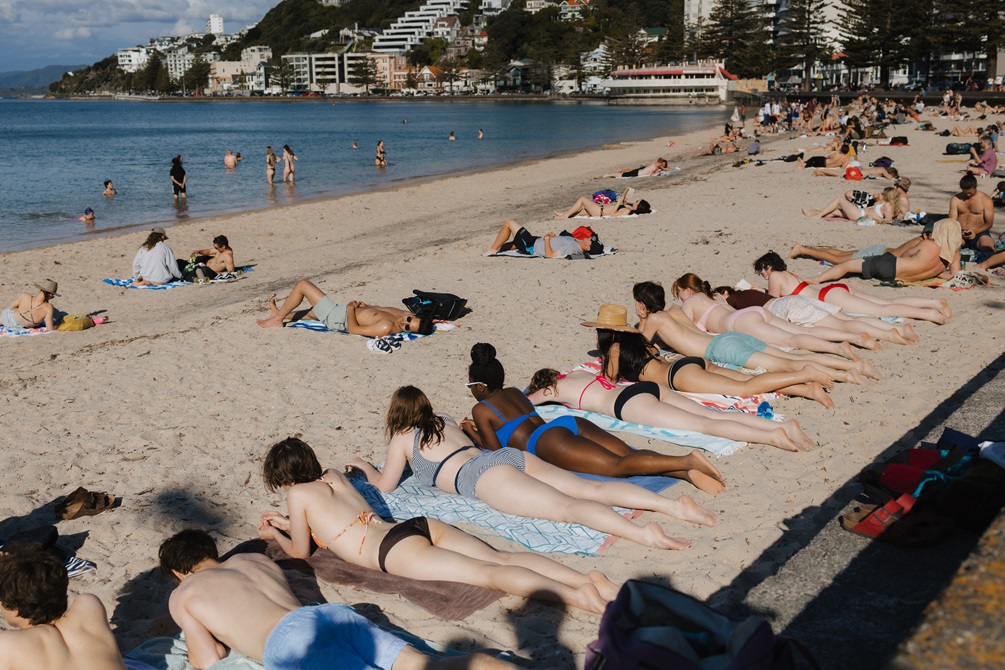 A long row of young people sunbath on a busy beach wearing their colourful bikinis on a summer's day.