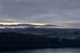 Wellington hills with houses dotted over one side. Still water and some light peeking through the clouds.