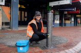 Person scrubbing down bollards with a blue bucket infront of them.