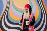 Woman wearing a pink high vis vest holding onto a paint brush and canister infront of a mural.