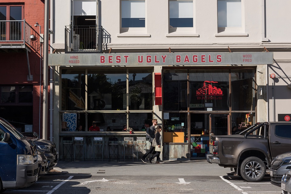 Two people walking down the street with Best Ugly Bagels in the background.