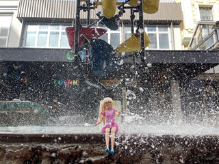 A barbie doll wearing a pink dress sitting on a ledge of a fountain with droplets raining down on her.