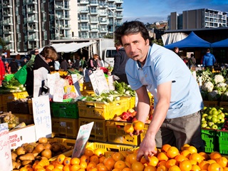 Man wearing a blue tshirt picking up oranges at a market.