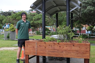 Man standing next to a wooden planter box wearing a green shirt and beanie.