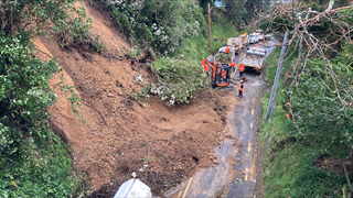 A birds eye view of a roading crew in orange high-vis working to clear a large slip off a road.