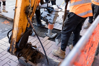 An infrastructure worker using heavy machinery to drill into the footpath.
