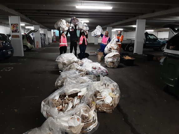 Group of people standing behind bags of rubbish in a carpark.