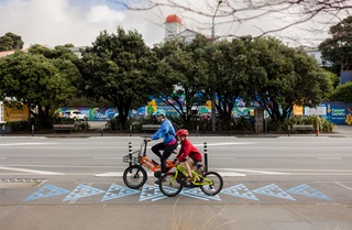 Two people riding a bike over blue markings on the ground.