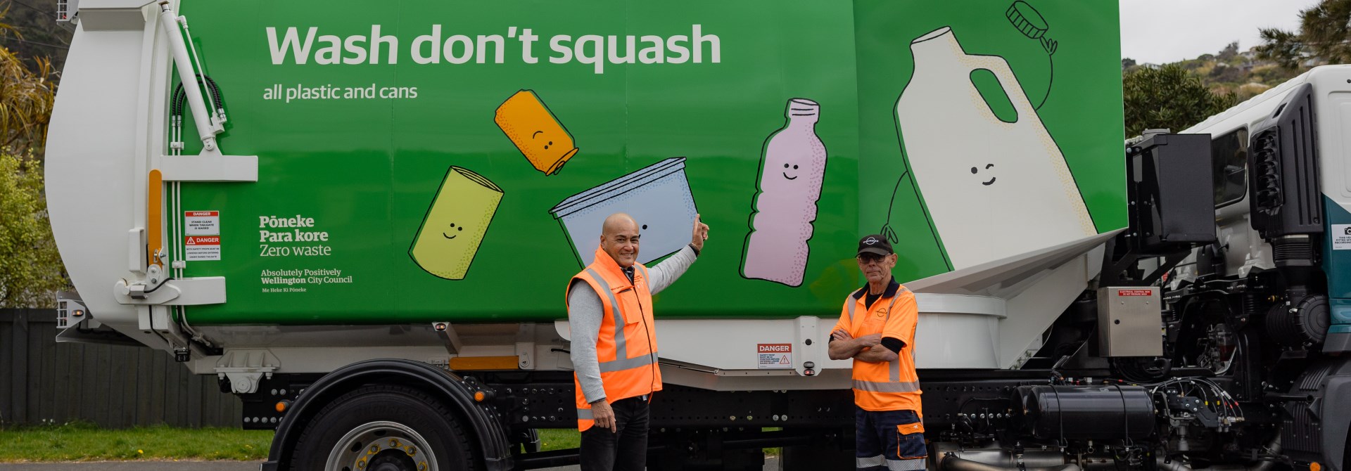 Two people wearing high vis jackets standing infront of a recycling truck.