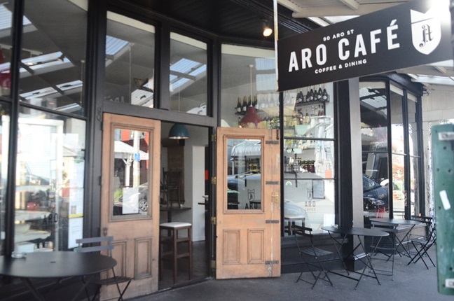A cafe on the side of the road with brown doors and a sign above it reading 'Aro Cafe'.