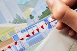 A hand using a small paintbrush to paint a watercolour painting of an outdoor pool.