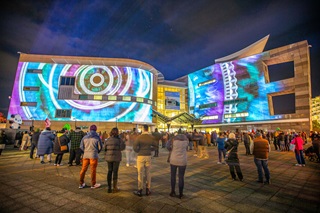 Light projections on a large building with a crowd standing infront.
