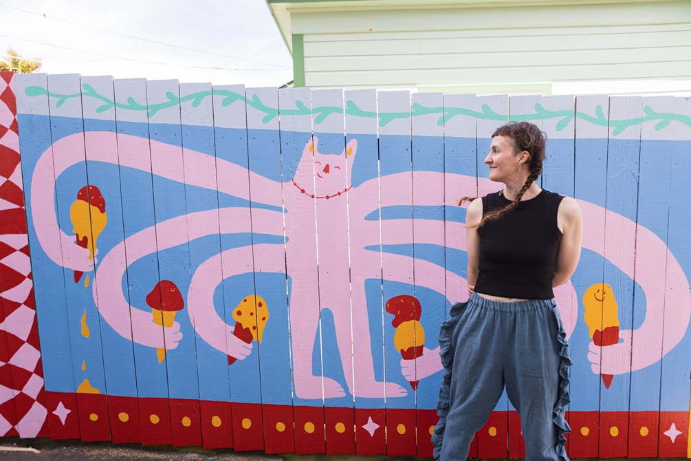 Person standing infront of a mural with a pink creature holding icecreams.