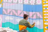 Person painting a mural on a fence.