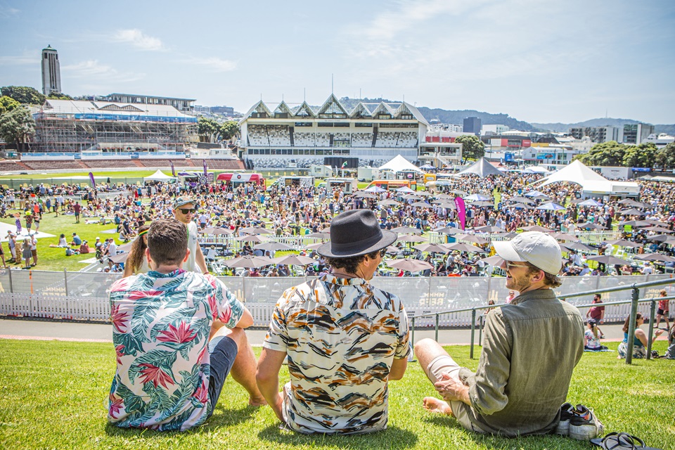 Group sitting on bank watching Beers at Basin in front of them with grandstand in background.