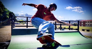 Man in a red tshirt and blue jeans, skating on a green ramp.