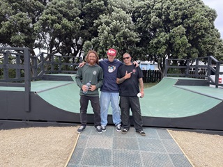 Three men standing together infront of a green skateboard ramp.