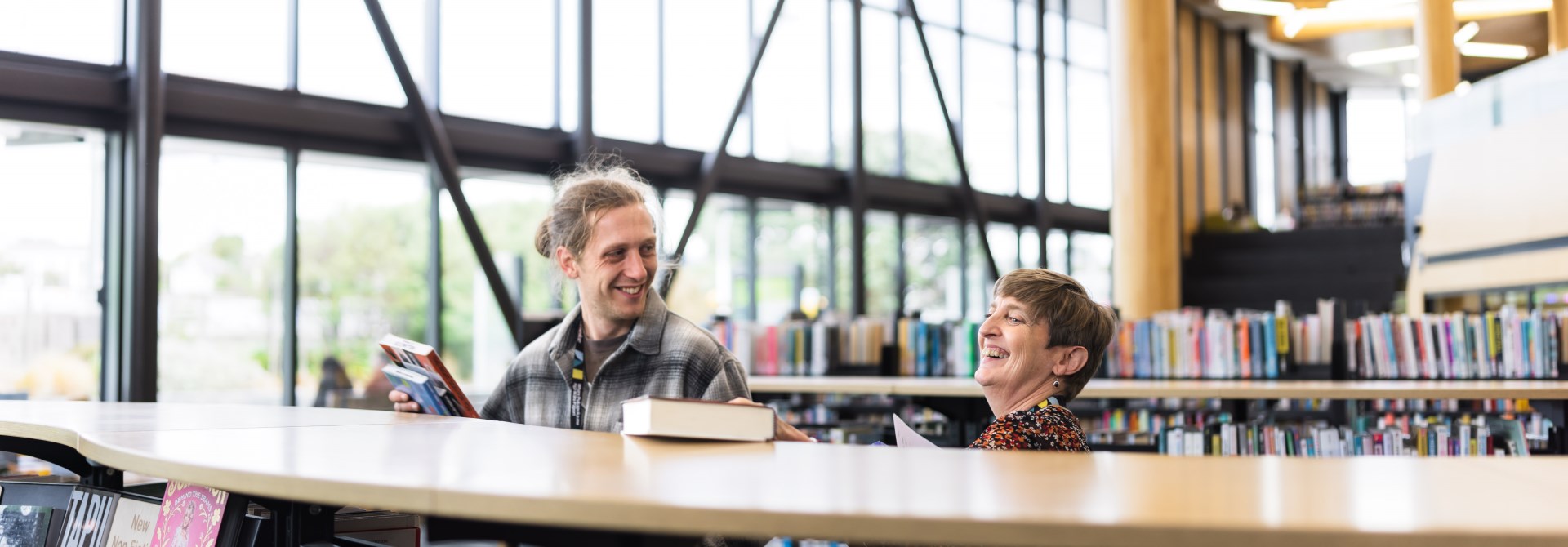 Two people laughing next to book shelves.