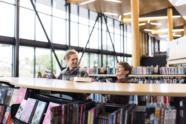 Two people laughing next to book shelves.