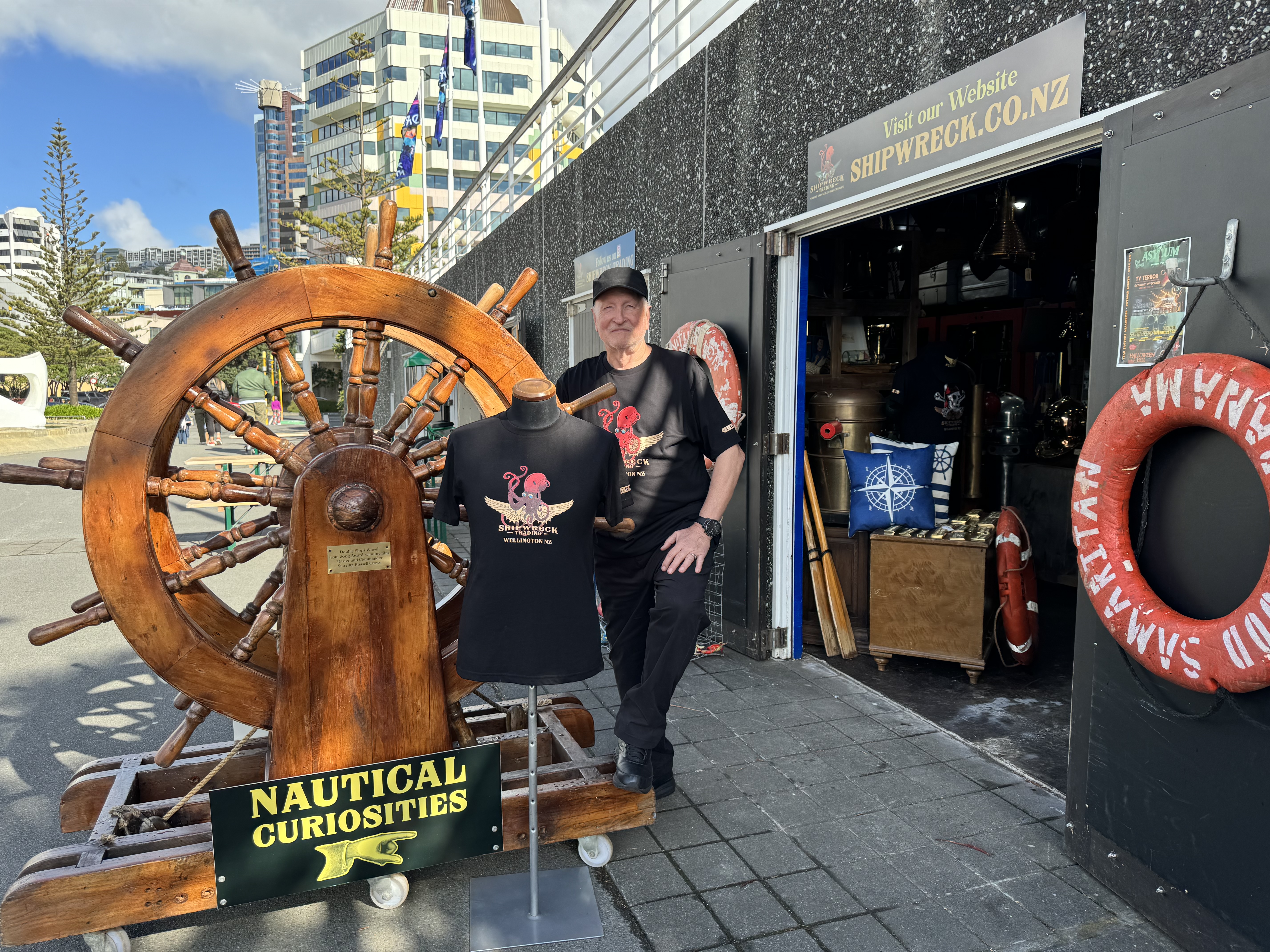 Man standing infront of a giant wheel outside his shipwreck themed shopfront.