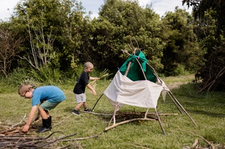 Two kids playing outdoors and building a teepee out of sticks.