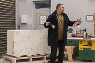 Man in a black coat holding sculpting tools.