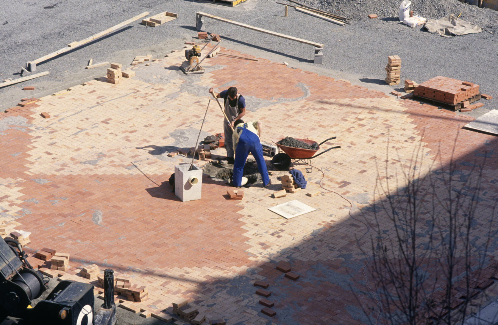 Two construction workers putting down tiles in the middle of Te Ngākau Civic Square.
