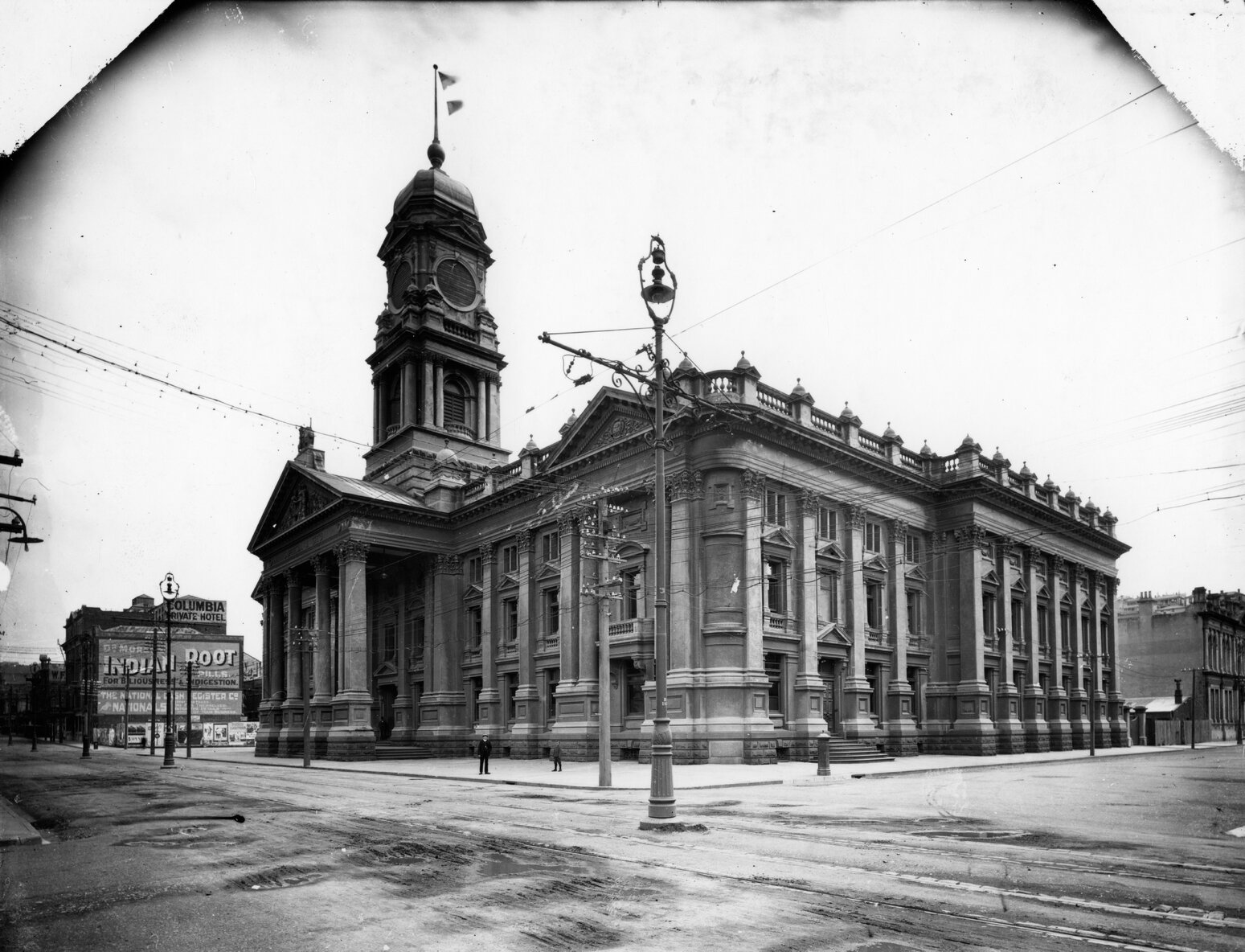 image of Town Hall in 1904, with original clocktower Elaborate street lamp in foreground. A sign for the Columbia Private Hotel is in the background, and an advertisement for Indian Root Pills (for indigestion)