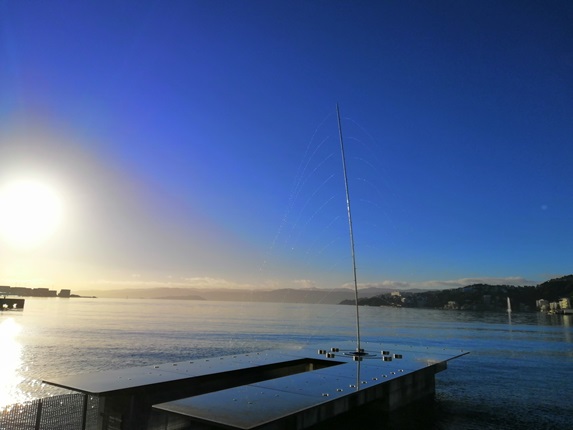 Len Lye's Water Whirler artwork whirling water around platform with sun rising across the harbour.