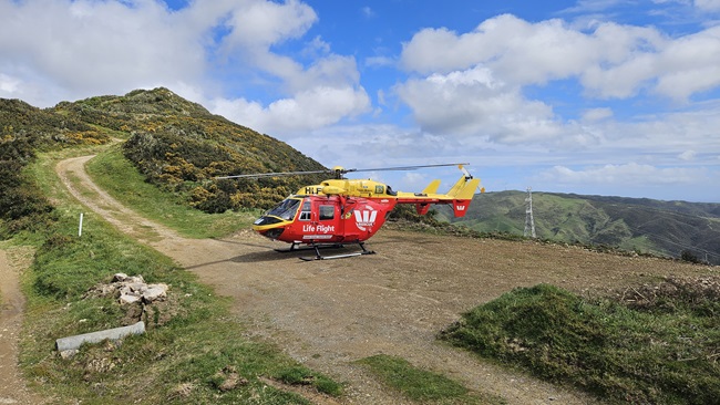 Red and yellow helicopter at the top of a hill with a path leading up to the landing area.