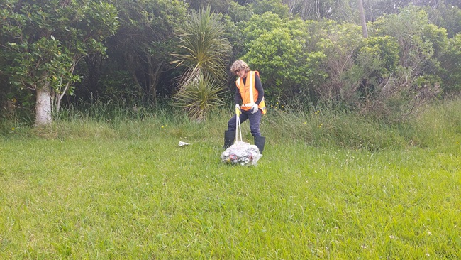 A man in high vis pulling a bag of rubbish across grass.