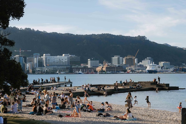 Oriental bay beach with crowds of people on it and the harbour in the background.