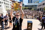 The All Blacks captain holding up the Rugby World Cup with a large crowd behind him.