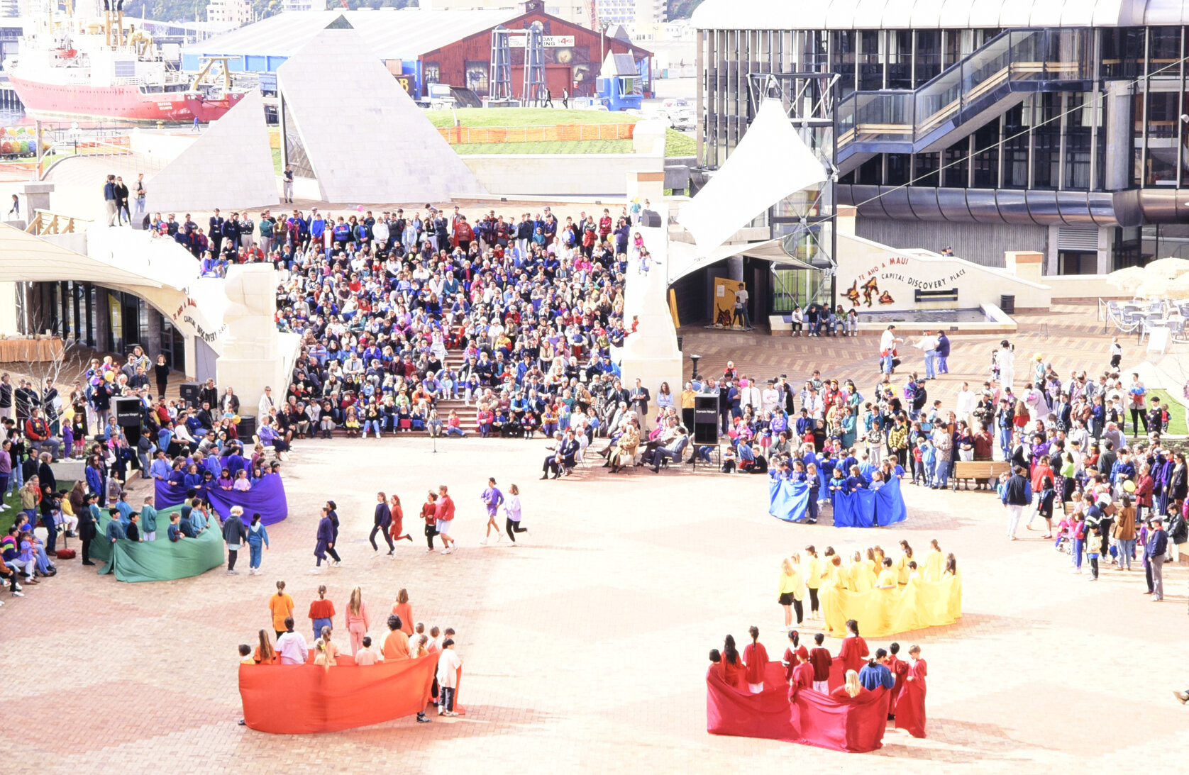 Events happening in civic square with small pockets of people running around while crowds watch on.