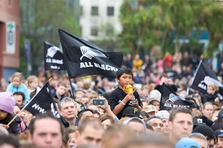 A crowd of All Blacks fans waving flags in the air.