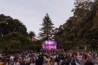 Stage in the background with performers on it and crowds of people gathered in front.
