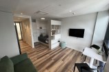 Studio apartment with a green couch in the foreground and a single bed with a tv and two person table.