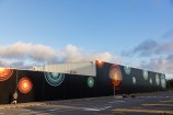 A series of giant gold, blue and green auripo rippling out across a 100-metre black wall.