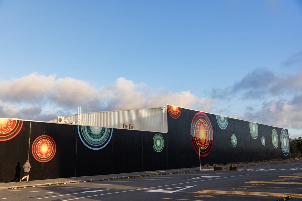 A series of giant gold, blue and green auripo rippling out across a 100-metre black wall.